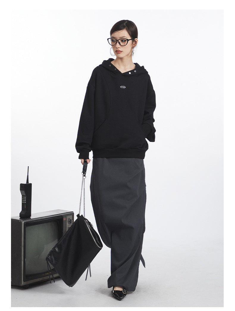 Black snap-detail hoodie with curved seam design, shown with floor-length gray skirt and chain-strap handbag