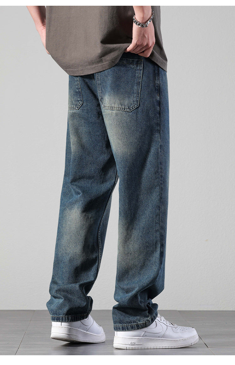 A person wearing relaxed fit washed denim jeans with silver chain bracelet and oversized gray t-shirt, viewed from back showing loose silhouette