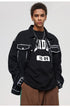 A man is standing against a gray background wearing a black SANHOMME outline denim jacket, graphic tee, and loose brown pants