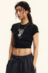 Model wearing a black cropped T-shirt with a graphic design and matching dark sweatpants, accessorized with a gold necklace and sunglasses