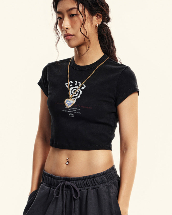 Model wearing a black cropped T-shirt with a graphic design and matching dark sweatpants, accessorized with a gold necklace and sunglasses
