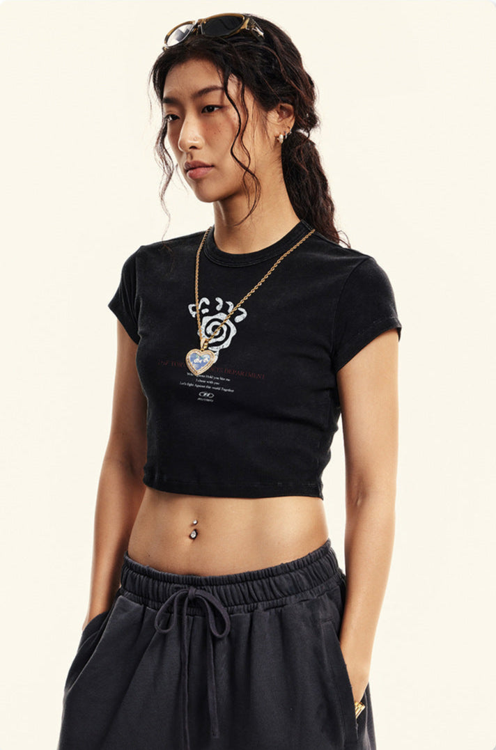 Model wearing a black cropped T-shirt with a graphic design and matching dark sweatpants, accessorized with a gold necklace and sunglasses