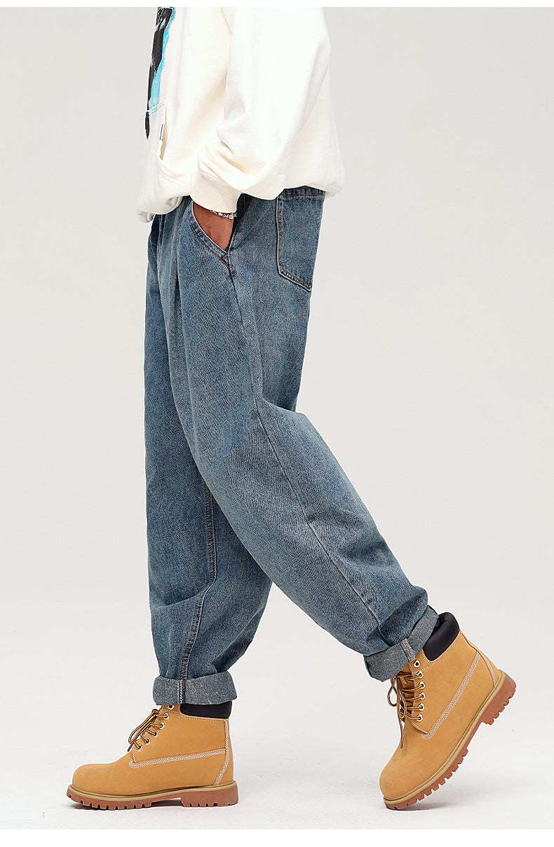 Side view of model wearing loose balloon-fit jeans with cuffed ankles, white sweatshirt and tan boots against white background