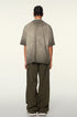 Back view of model with braided hair in taupe-washed oversized t-shirt and olive cargo pants, showing distressed collar detail
