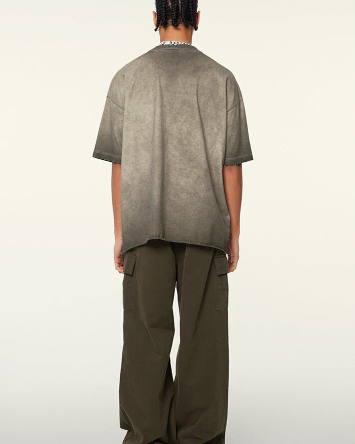 Back view of model with braided hair in taupe-washed oversized t-shirt and olive cargo pants, showing distressed collar detail