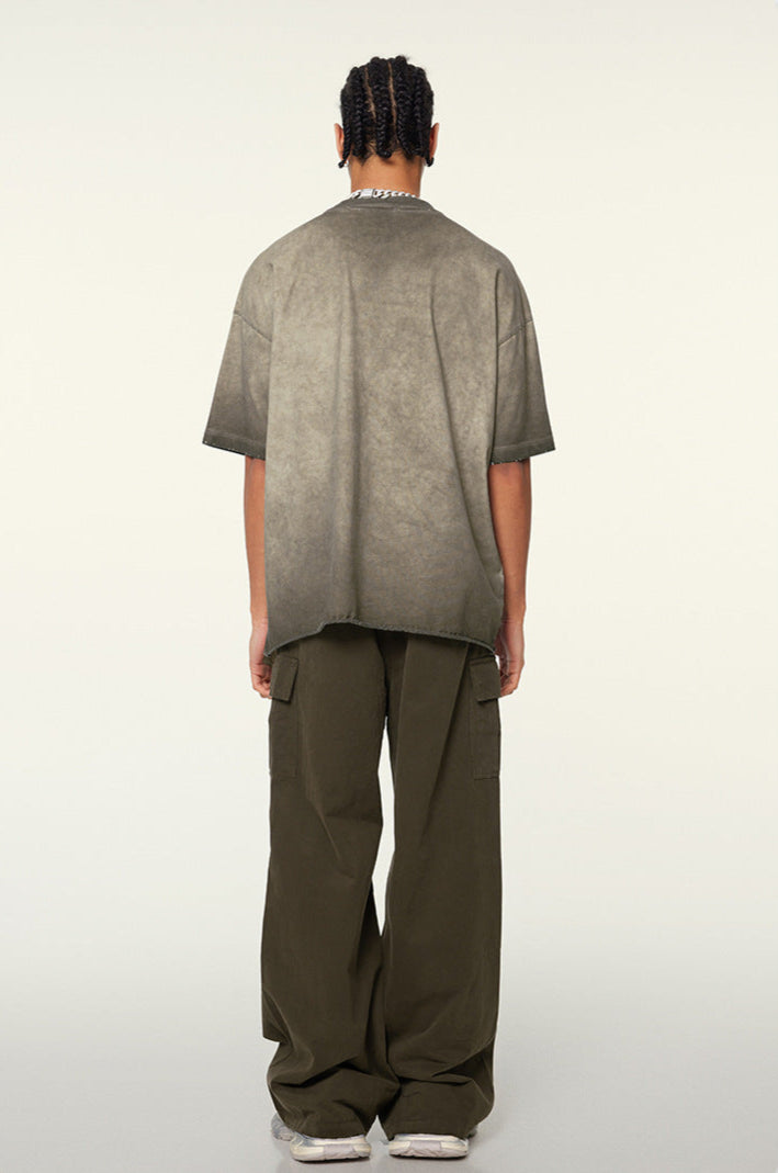 Back view of model with braided hair in taupe-washed oversized t-shirt and olive cargo pants, showing distressed collar detail