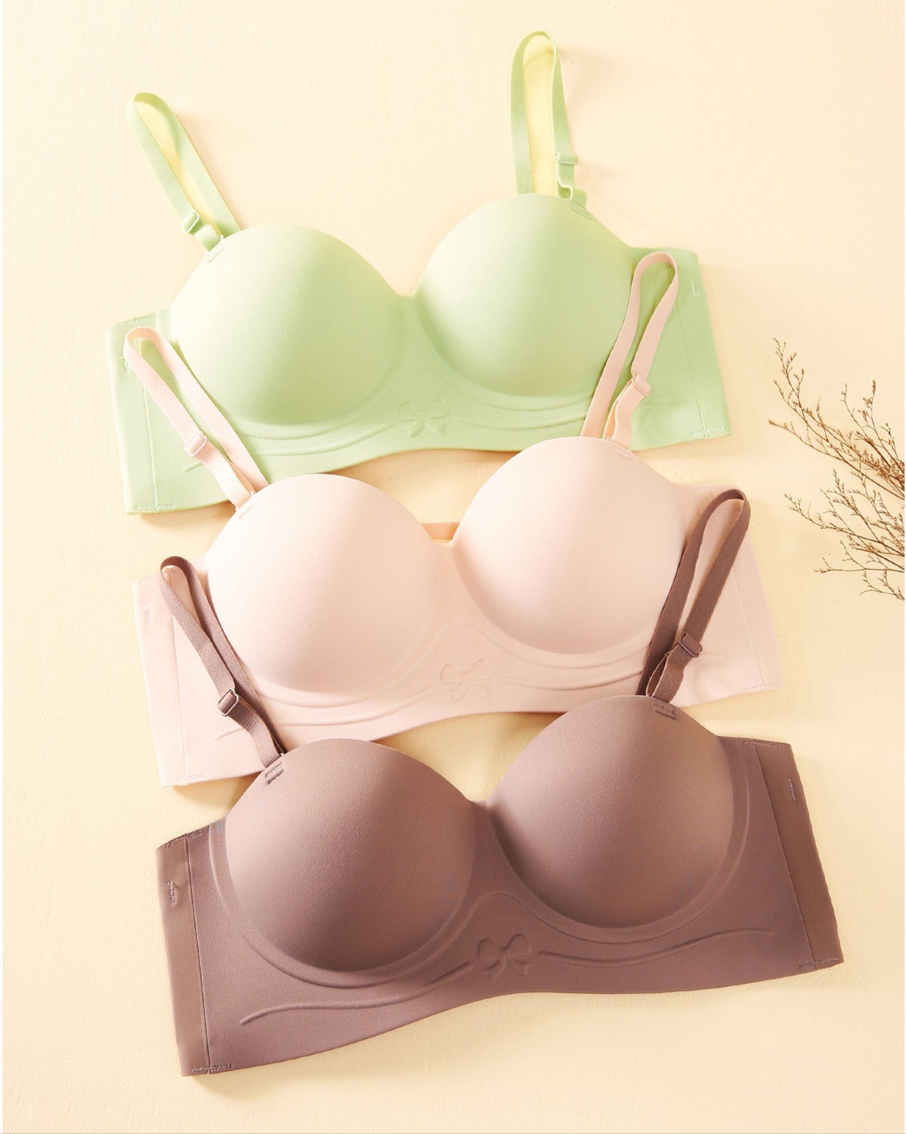 Three bras in green, pink, and coffee arranged on a soft beige background, showcasing color variety and seamless design.