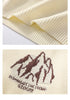 Close-up of cream sweater showing ribbed hem and brown mountain logo embroidery