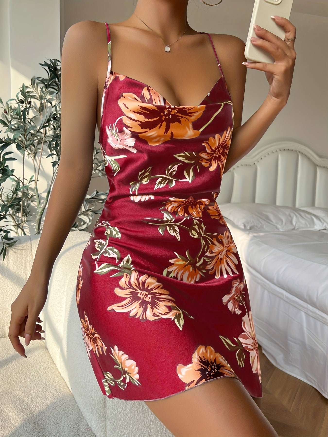 A model wearing burgundy floral print satin slip dress with cowl neckline, taking mirror selfie in bedroom setting