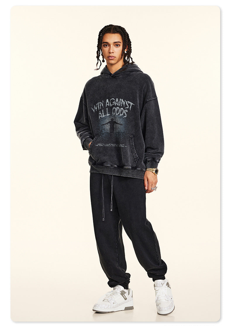 Model in black graphic hoodie and white sneakers, standing in studio with braided hair and chain necklace