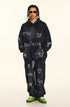 Model wearing black version of graffiti sweatsuit with white painted designs, green sneakers and gold-framed sunglasses