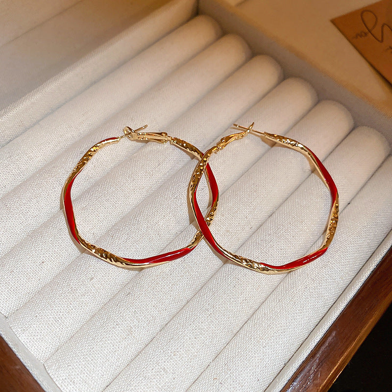 A pair of hammered gold and red enamel hoop earrings is displayed on a jewelry tray with a wooden frame