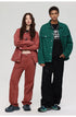 A woman with arms crossed in rust denim set poses with man wearing green denim jacket over black tee and pants