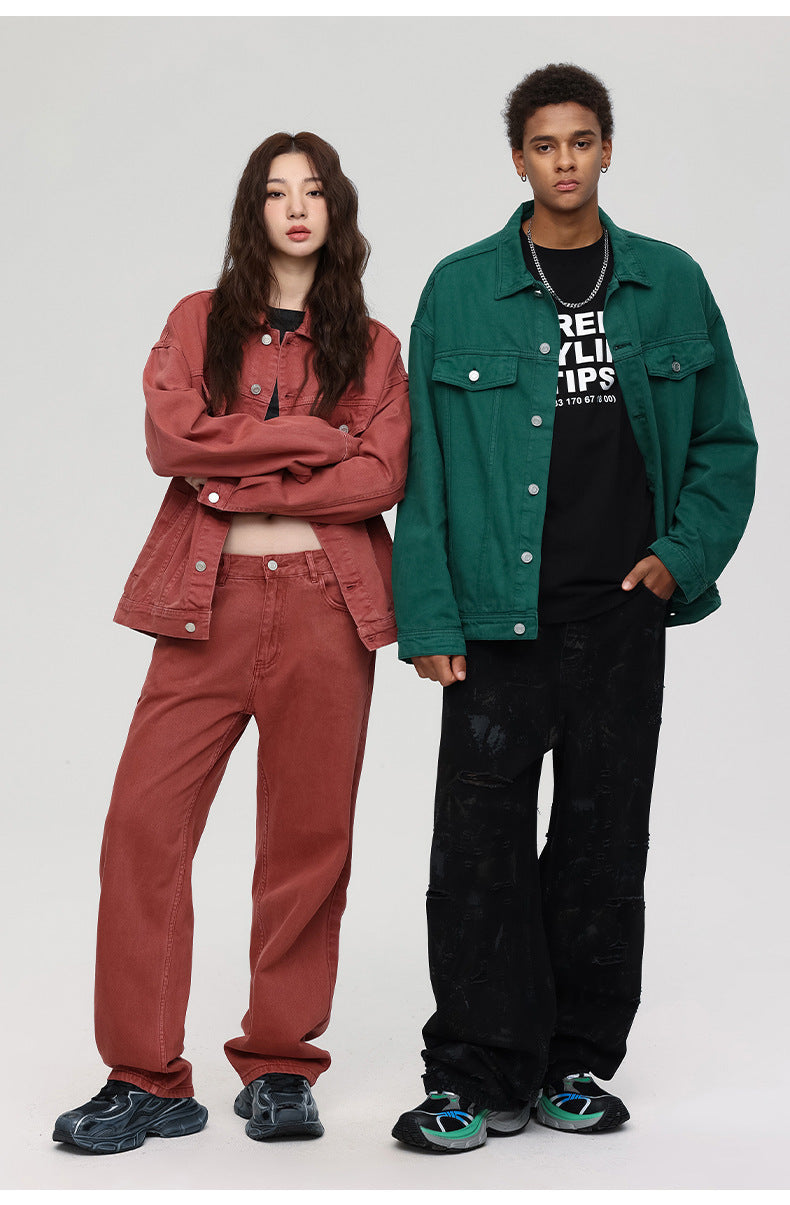 A woman with arms crossed in rust denim set poses with man wearing green denim jacket over black tee and pants