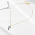 A gold chain necklace with blue sapphire cross pendant displayed flat on white minimalist background