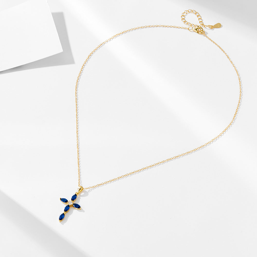 A gold chain necklace with blue sapphire cross pendant displayed flat on white minimalist background