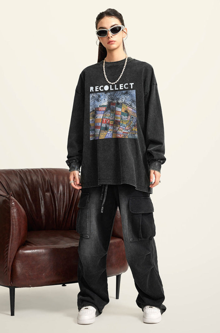 A female model wears a black oversized "RECOLLECT" sweatshirt, black cargo pants, and sneakers, standing in front of a leather chair