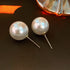 Pearl stud earrings on dark surface with decorative glass in background casting warm shadows