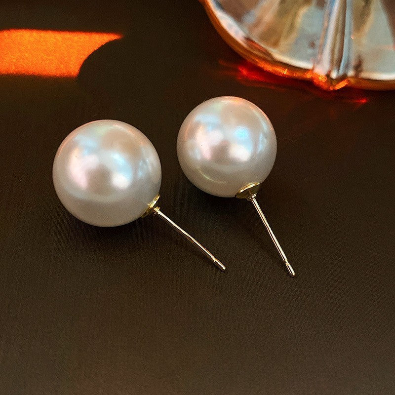 Pearl stud earrings on dark surface with decorative glass in background casting warm shadows
