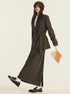 Side profile of brown suit set featuring belted blazer, maxi skirt and two-tone leather handbag