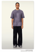 Model with braided hair wearing slate blue t-shirt and black wide-leg pants with silver chain necklace against cream background