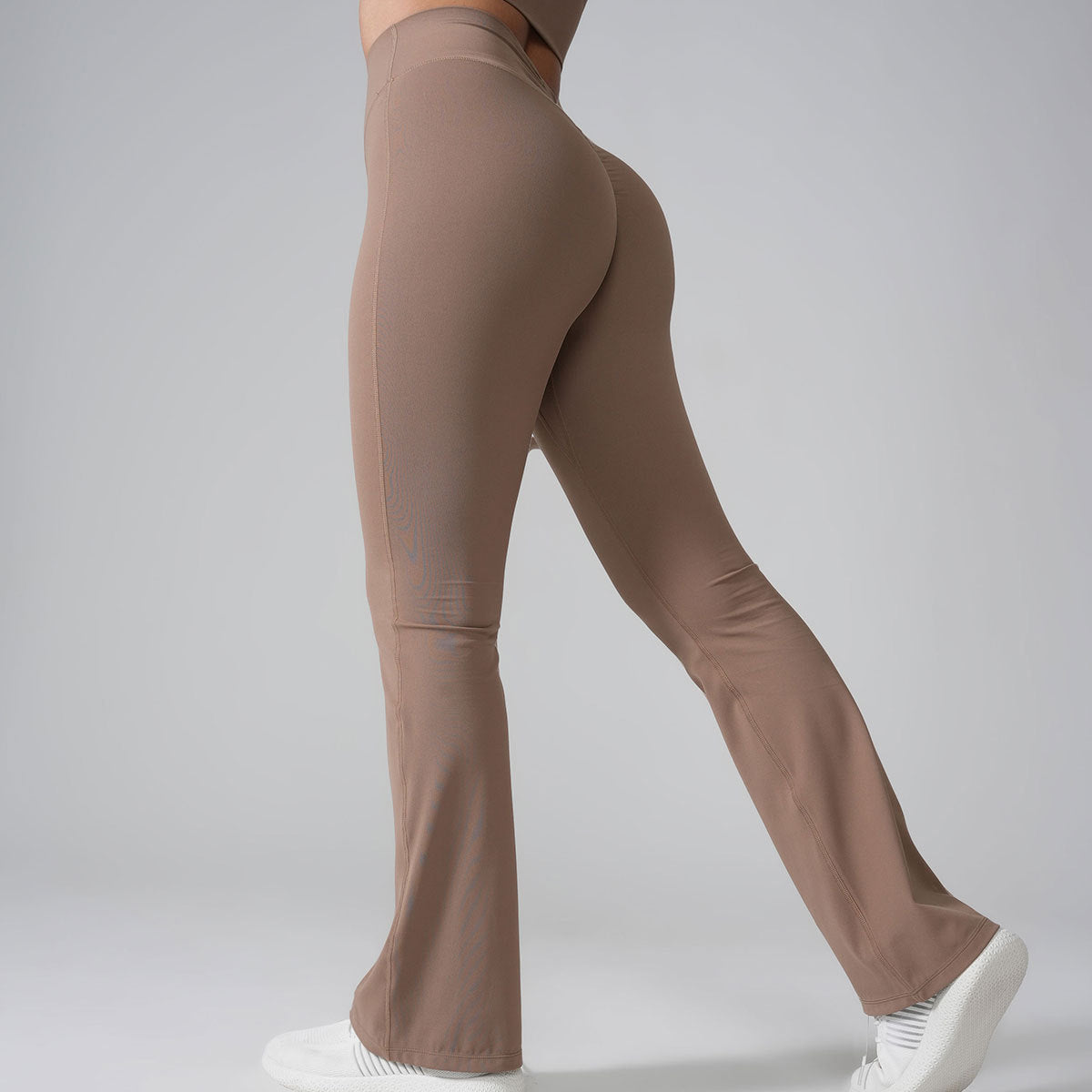 Close-up side view of taupe flared yoga pants with white sneakers, highlighting leg silhouette against gray background