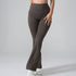 A model wearing high-waisted brown flared yoga pants with white sneakers, photographed against a gray background