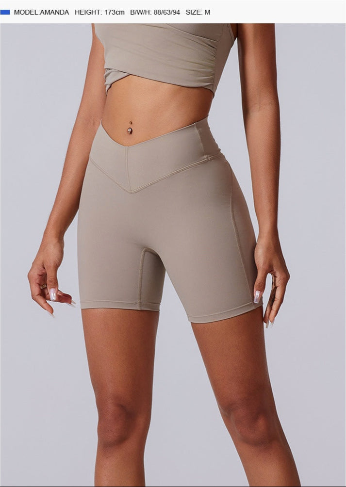 A model is standing wearing beige high-waisted V-cut compression shorts with matching crop top, product dimensions displayed above