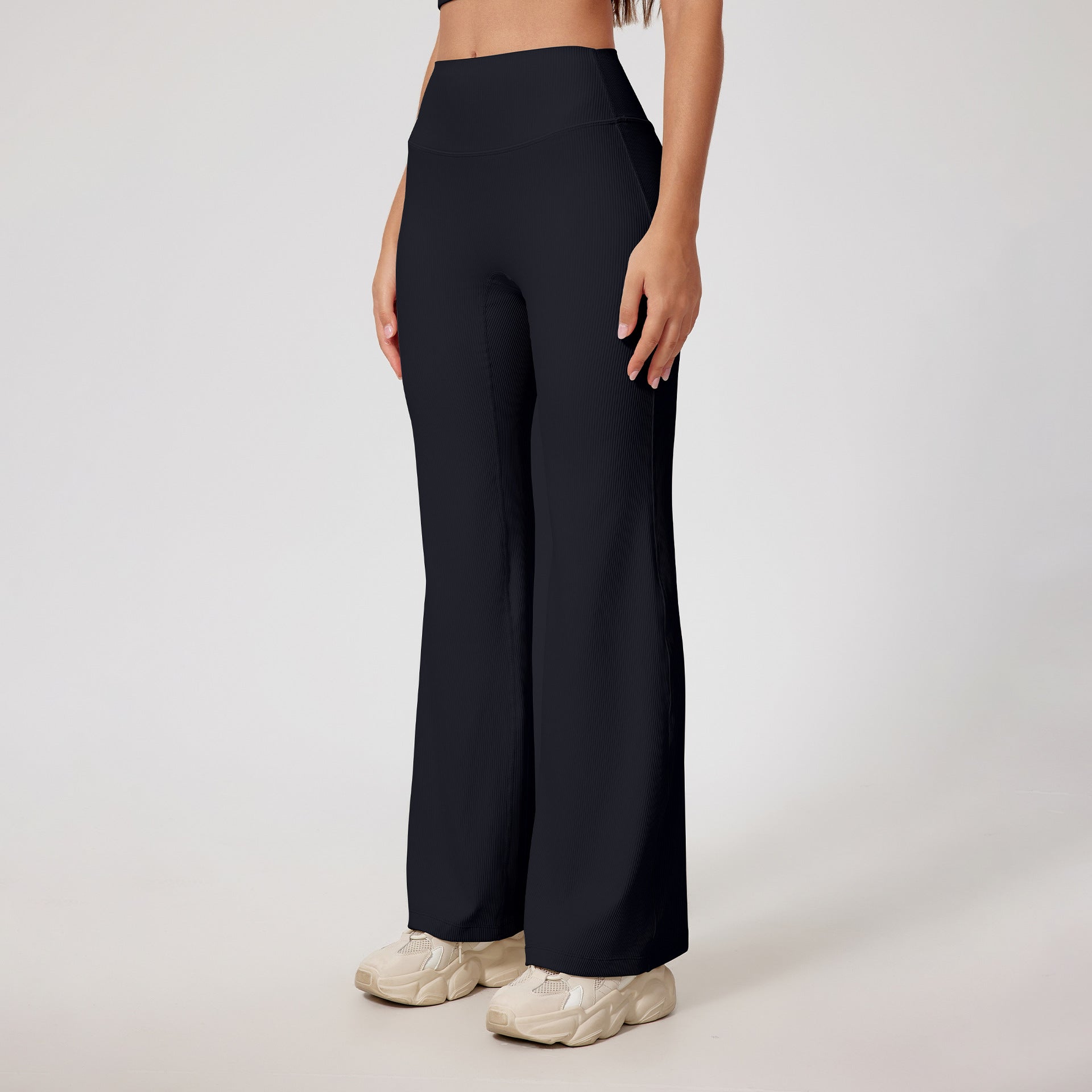 Black ribbed yoga pants with high waist, flared leg design, athletic wear fabric, neutral chunky sneakers, minimalist styling