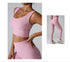 A woman wearing a pink ribbed scoop neck sports bra with hand on hip paired with matching high-waisted leggings and white sneakers against a gray backdrop