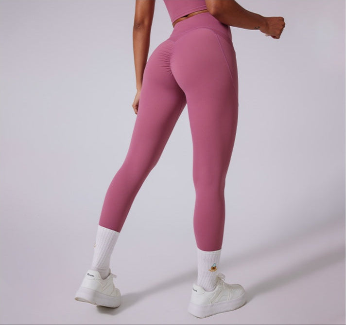Model wearing dusty rose athletic leggings with ruched back detail, paired with matching crop top and white sneakers