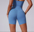 A model is showing back view of blue seamless biker shorts with high-waisted design and supportive compression fit against neutral backdrop