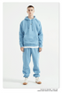 Male model wearing light blue sweatsuit with silver pendant necklace against white background