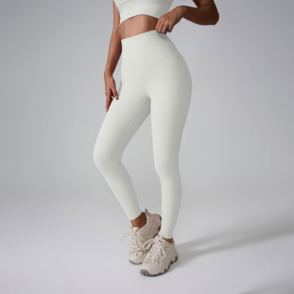 A model wearing off-white high-waisted workout leggings and matching crop top against gray studio background
