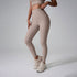 A model wearing beige high-waisted workout leggings and matching crop top against gray studio background