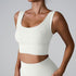 A woman wearing an ivory ribbed scoop neck sports bra with wide straps and contoured underbust support paired with matching bottoms against gray background