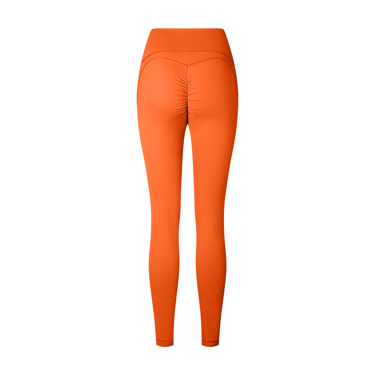Product photo of bright orange athletic leggings with ruched center seam and high waistband on white background