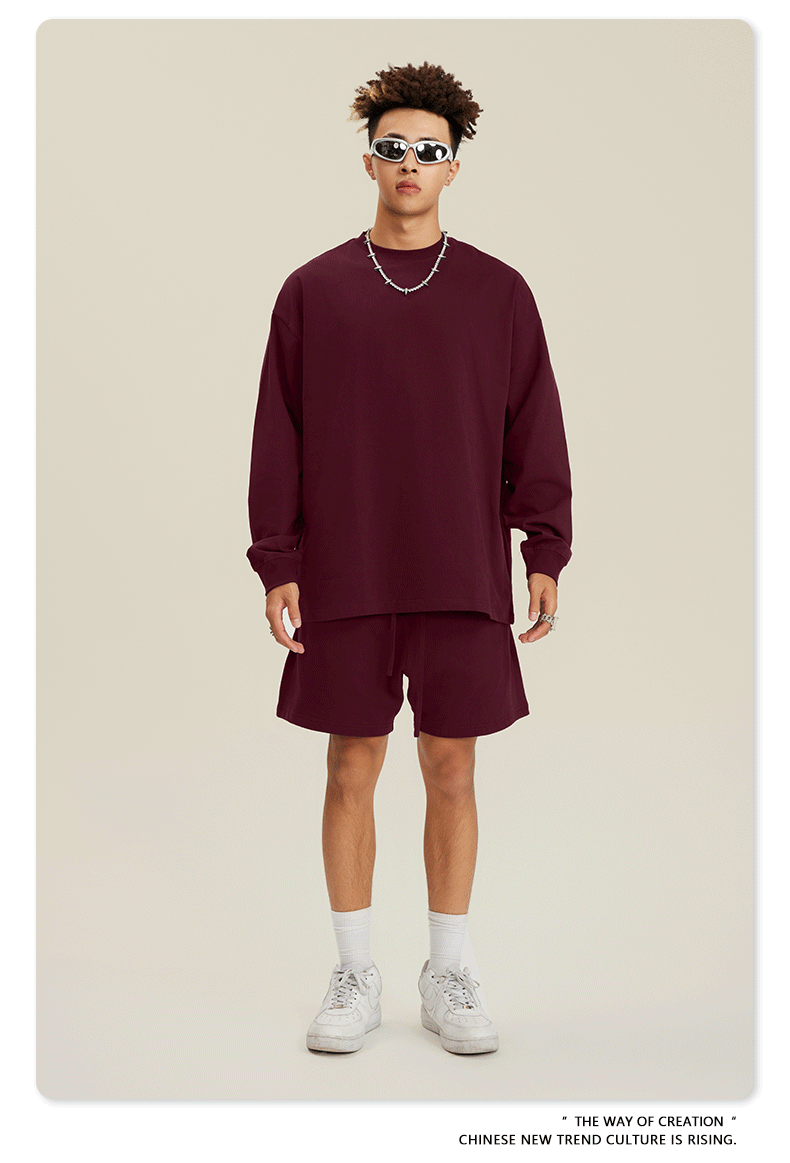 Man in burgundy sweatshirt and shorts set with sunglasses, chain necklace and white sneakers