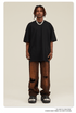 Model with dreadlocks wearing black oversized t-shirt with brown distressed jeans and black footwear against beige background