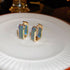 Gold hexagonal hoop earrings with blue-green gemstone accents arranged on white plate displaying contemporary jewelry styling