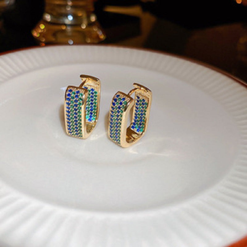 Gold hexagonal hoop earrings with blue-green gemstone accents arranged on white plate displaying contemporary jewelry styling