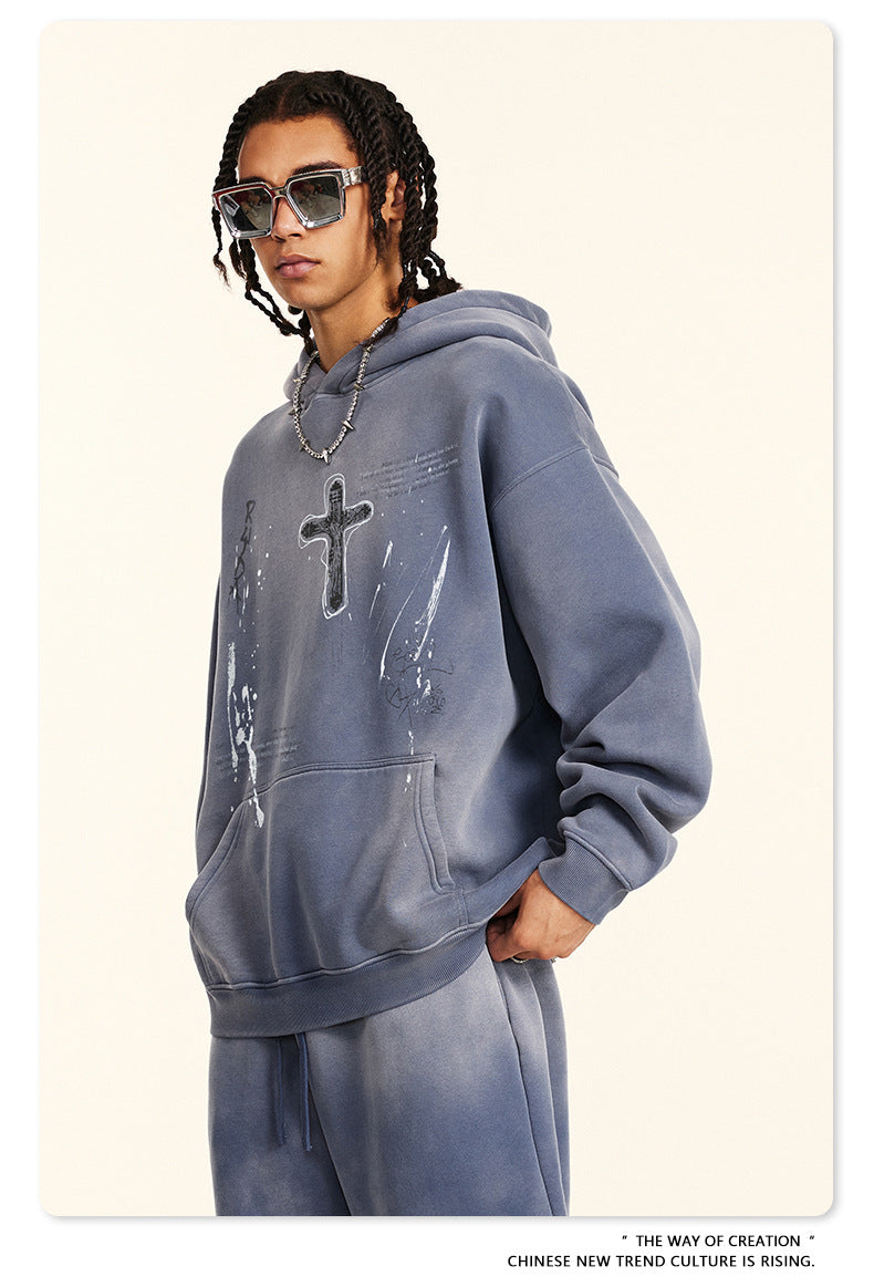 Oversized gray hoodie featuring cross graphic design and sketch details, worn with matching sweatpants and square sunglasses