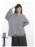 Close-up view showcasing grey cable-knit sweater's textured pattern and distressed hem detail, layered over striped shirt and paired with charcoal skirt