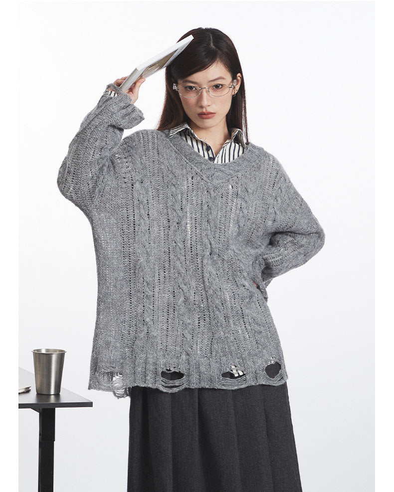 Close-up view showcasing grey cable-knit sweater's textured pattern and distressed hem detail, layered over striped shirt and paired with charcoal skirt