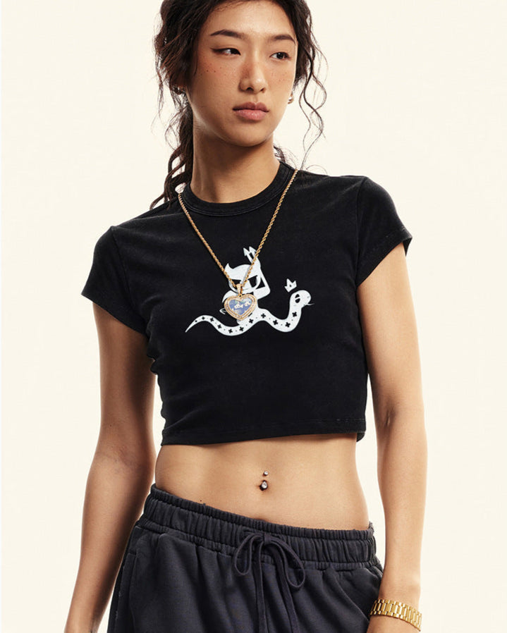Black cropped t-shirt featuring a white devil girl and snake graphic, worn with black sweatpants and accessories