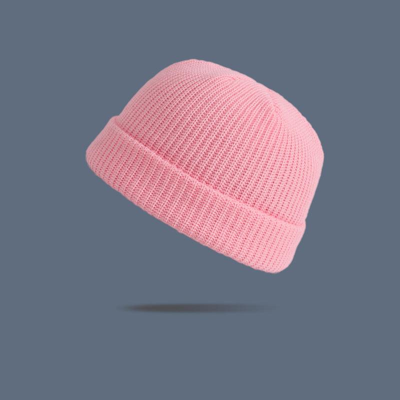 A pink ribbed knit beanie with folded cuff floating against slate gray background, displaying soft feminine winter hat style