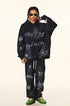 Model in black graffiti hoodie and sweatpants with white painted symbols, adjusting gold sunglasses against neutral background