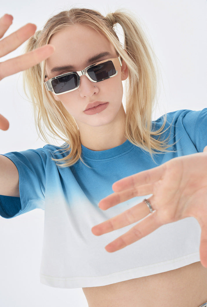 Side view of model with sunglasses, pulling hair and sticking out tongue, wearing blue ombré cropped t-shirt