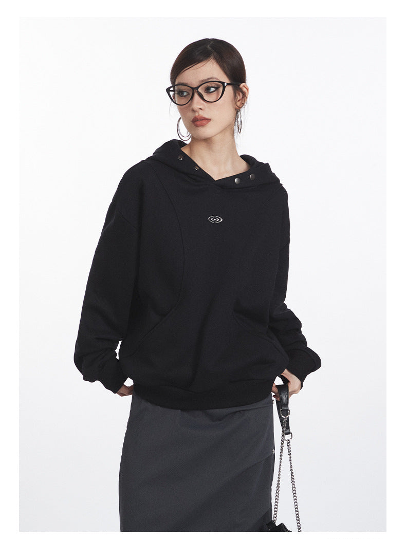 Close-up detail of black cotton hoodie showing metallic snap closures, embroidered eye logo, and kangaroo pocket