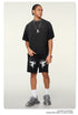 Streetwear outfit with oversized black t-shirt, cupid graphic shorts, silver chain necklace and chunky gray sneakers, styled with cornrow braids